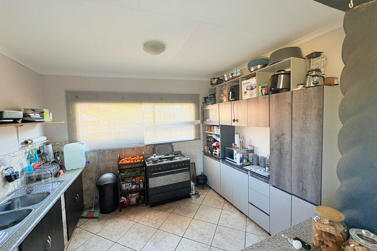 A functional kitchen featuring built-in cabinetry, a double bowl sink, tiled flooring, and a freestanding stove with a window providing natural light.