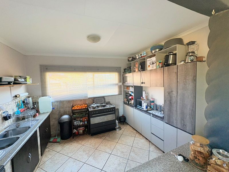 A functional kitchen featuring built-in cabinetry, a double bowl sink, tiled flooring, and a freestanding stove with a window providing natural light.