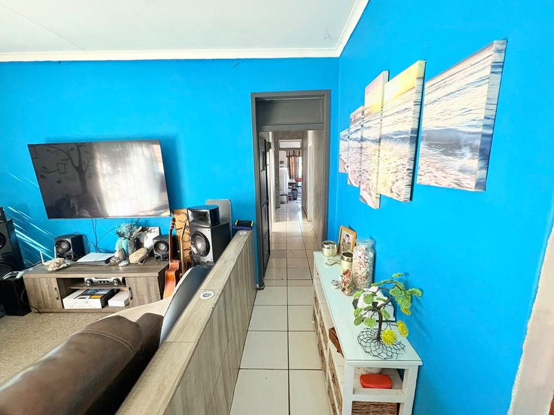 A living room area featuring tiled flooring and a partition wall, leading into a hallway.