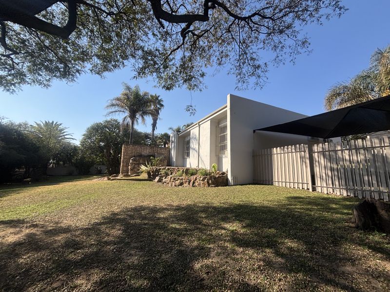 Rear view of the property featuring a landscaped garden, stone retaining wall, and a shaded outdoor area with perimeter fencing.