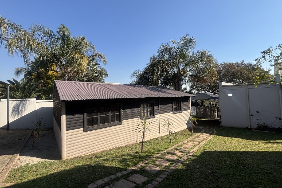 A well-maintained rear garden featuring a detached timber-clad structure with a corrugated metal roof and a paved walkway.