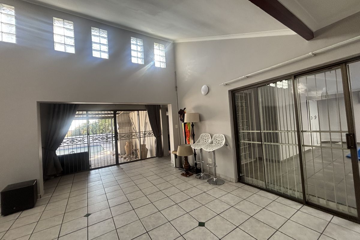 Spacious living area featuring high ceilings with exposed beams, tiled flooring, and large sliding glass doors providing access to the outdoor area.