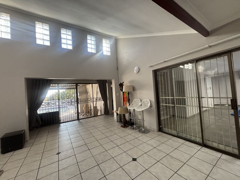 Spacious living area featuring high ceilings with exposed beams, tiled flooring, and large sliding glass doors providing access to the outdoor area.