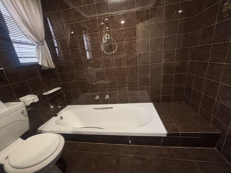 A bathroom featuring a built-in bathtub with dark brown wall and floor tiles, complemented by a standard toilet.