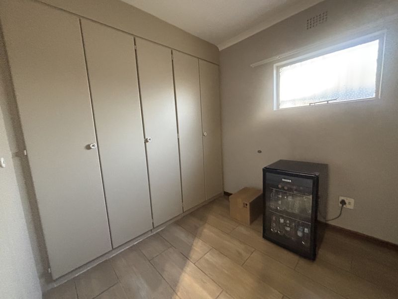 A bedroom featuring neutral-toned built-in cupboards, tiled flooring, and a small window, providing a clean and functional space ready for personalization.