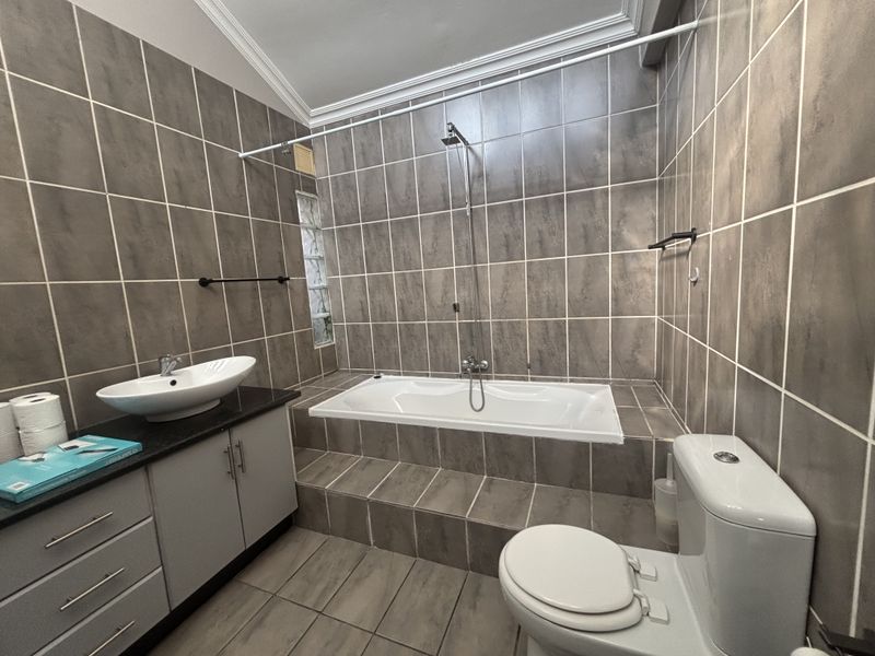 A modern bathroom featuring a built-in bathtub with shower attachment, a vessel sink vanity, and neutral tiled walls.