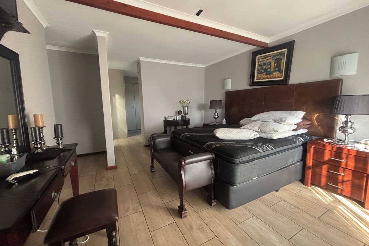 Spacious bedroom featuring tiled flooring, an exposed timber ceiling beam, and integrated wall lighting, providing a comfortable and well-maintained living space.