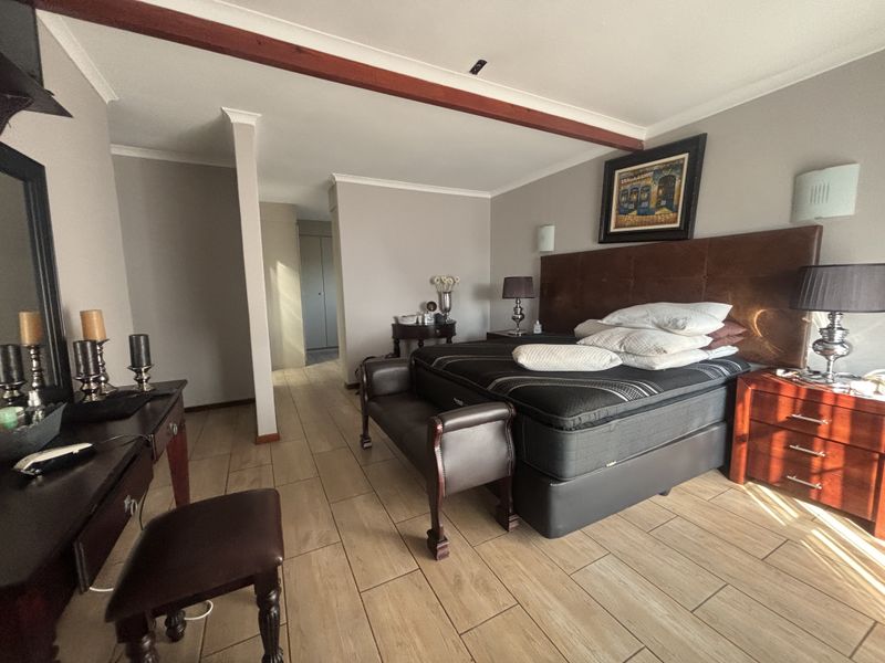 Spacious bedroom featuring tiled flooring, an exposed timber ceiling beam, and integrated wall lighting, providing a comfortable and well-maintained living space.