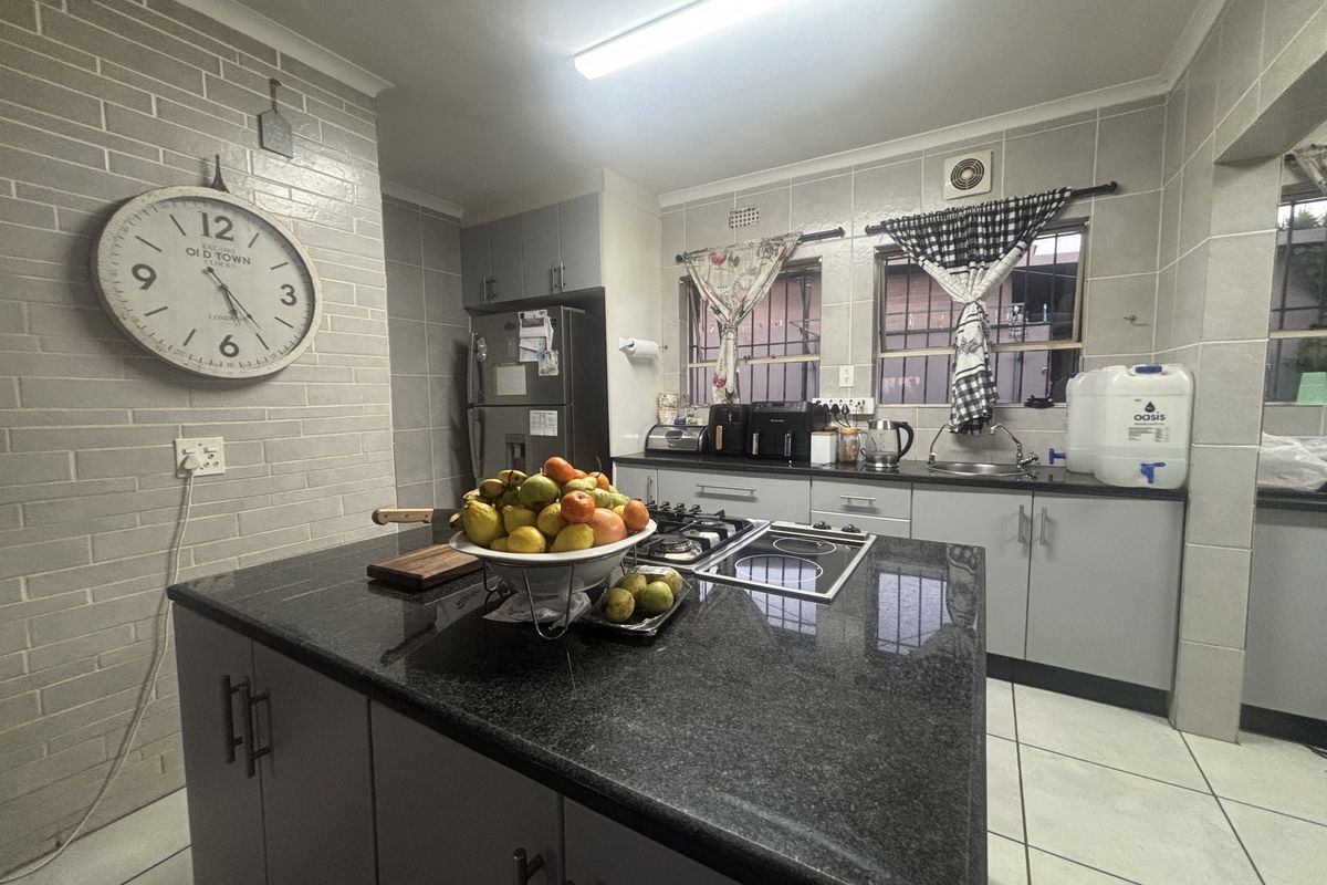 A functional kitchen featuring a central island with granite countertops, dual hobs, tiled finishes, and ample built-in cabinetry.