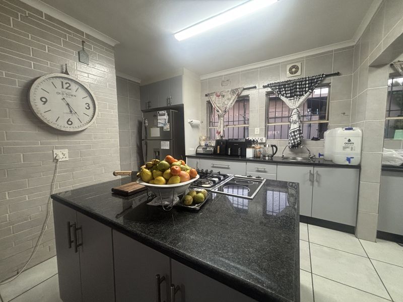 A functional kitchen featuring a central island with granite countertops, dual hobs, tiled finishes, and ample built-in cabinetry.