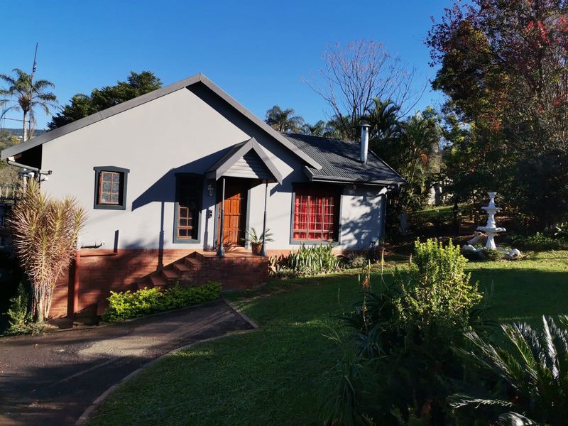 A charming single-story home featuring a grey facade with brick detailing, a corrugated metal roof, and a well-maintained front garden with a fountain.