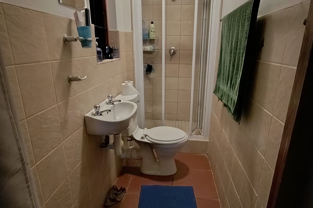 A compact bathroom featuring a shower enclosure, wall-mounted basin, and toilet with neutral wall tiling and terracotta-style floor tiles.