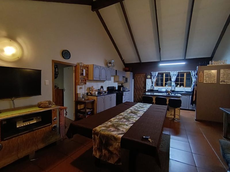 Spacious open-plan living and kitchen area featuring vaulted ceilings with exposed timber beams, tiled flooring, and a functional kitchen layout with an island.