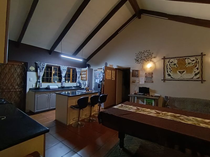 Spacious open-plan living area featuring a vaulted ceiling with exposed timber beams, tiled flooring, and a functional kitchen island with built-in cabinetry.