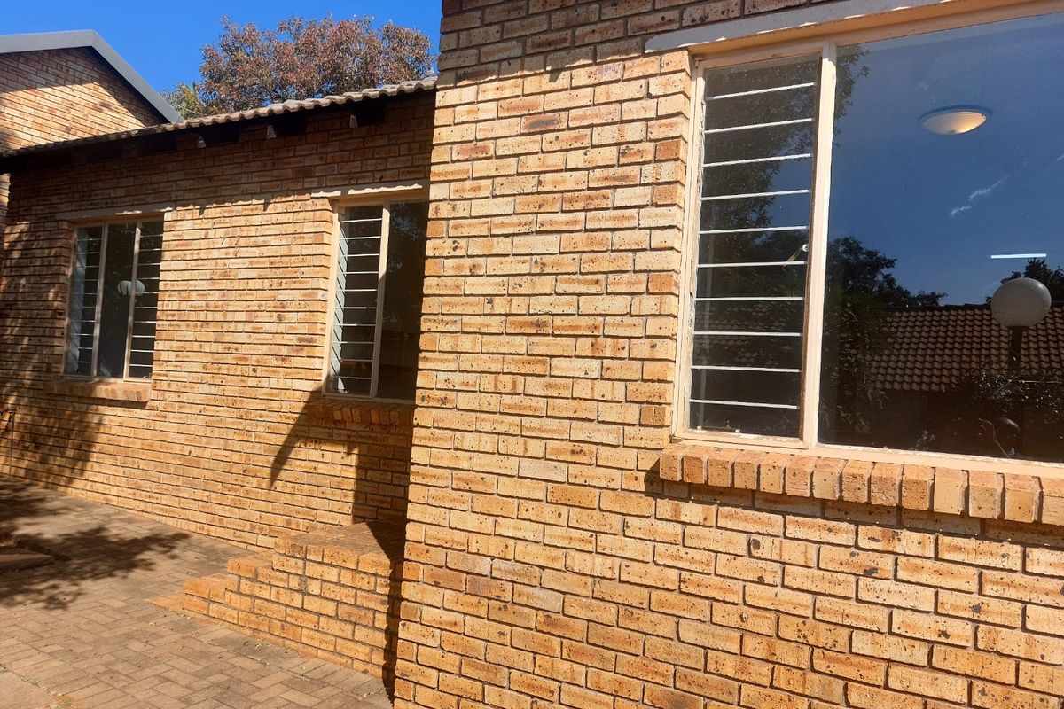 A view of the rear exterior featuring face brick walls, security bars on windows, and a paved patio area.