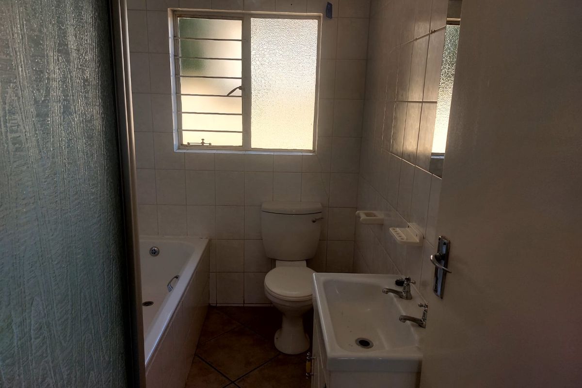 A functional bathroom featuring a bathtub, toilet, and vanity basin with tiled finishes and security bars on the window.