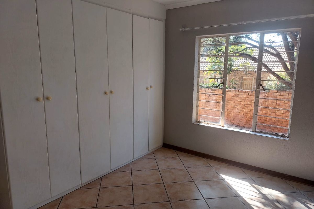 A bright, empty bedroom featuring built-in cupboards, tiled flooring, and security bars on the window.