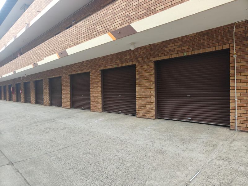 A row of secure, individual lock-up garages featuring brown roller shutter doors and a durable face brick exterior finish.