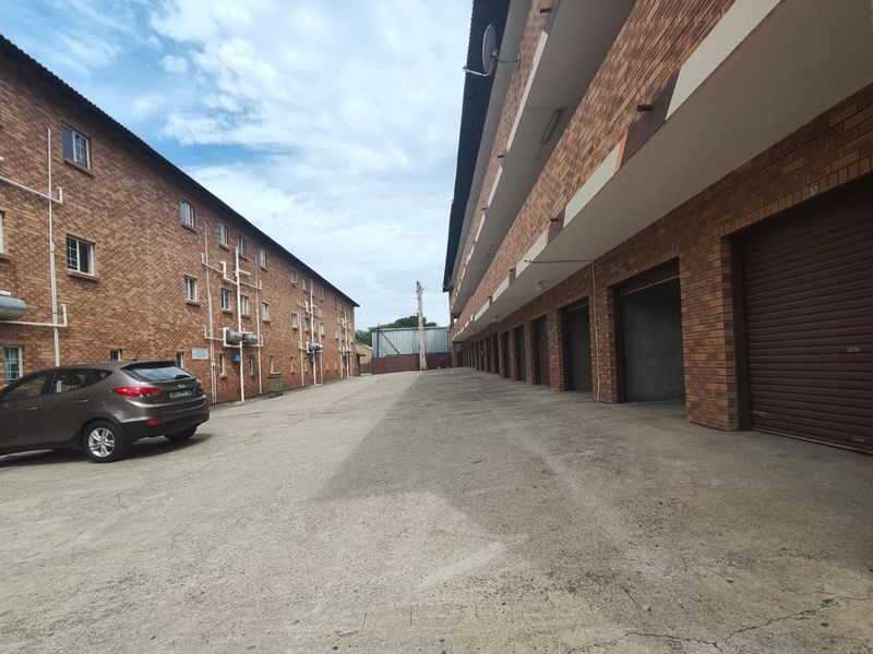Exterior view of an apartment complex featuring face brick facades, a paved driveway, and a row of ground-level roller shutter garages.