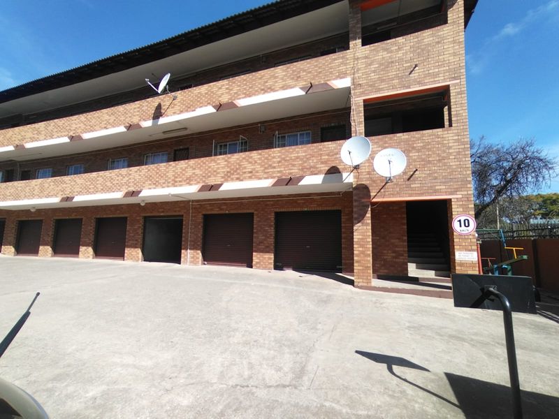 Exterior view of a multi-story apartment building featuring face brick construction, multiple garage units, and private balconies.
