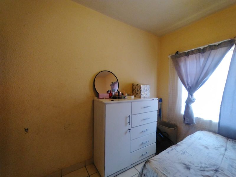 A bedroom featuring tiled flooring and a window, currently showing signs of wear on the wall surfaces.