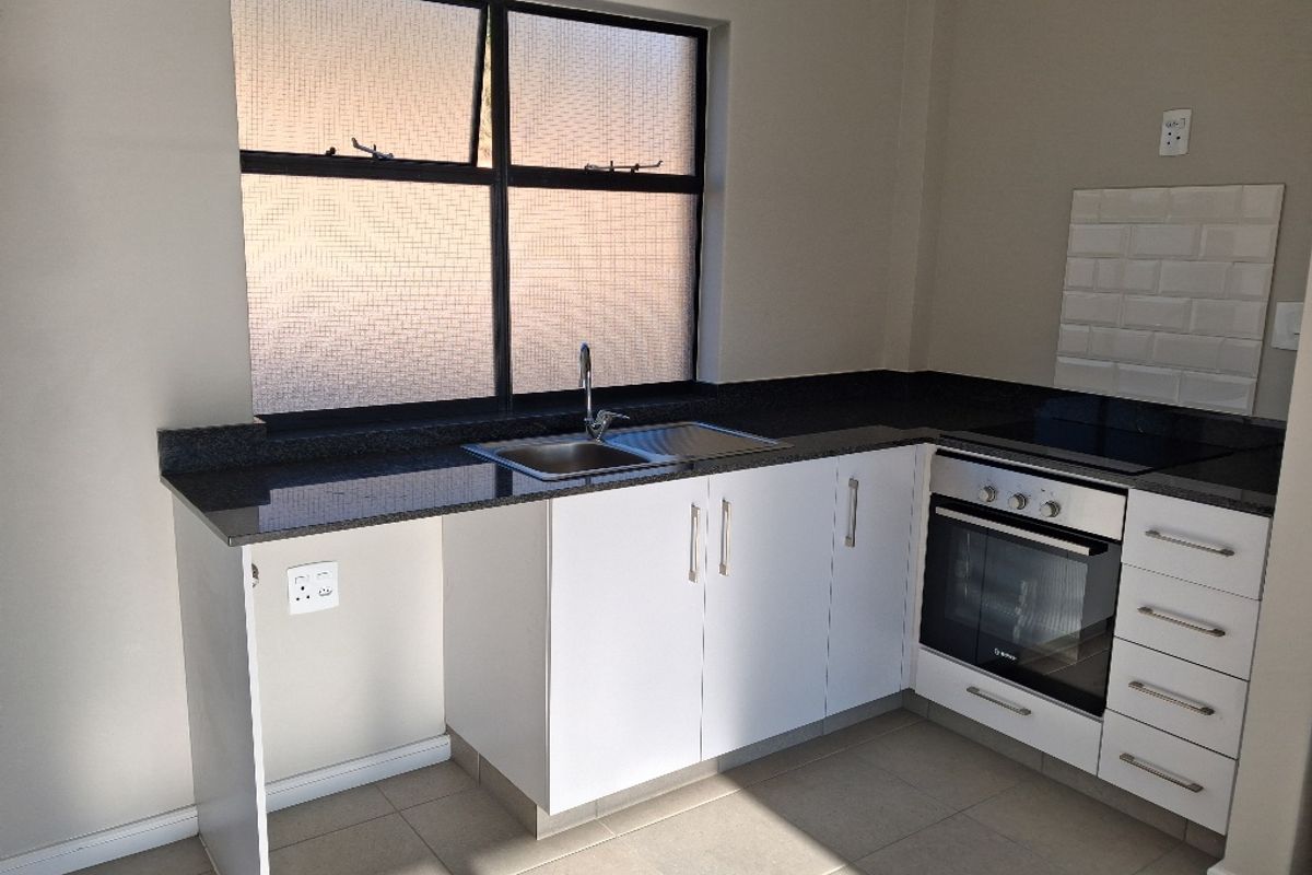 A clean, modern kitchen featuring granite countertops, built-in oven, ceramic hob, and white cabinetry with a tiled splashback and neutral floor tiles.