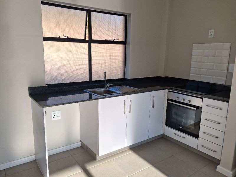 A clean, modern kitchen featuring granite countertops, built-in oven, ceramic hob, and white cabinetry with a tiled splashback and neutral floor tiles.