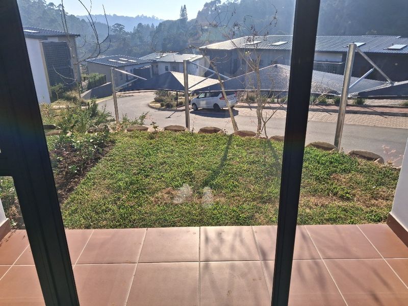 A view from a tiled patio looking out over a small garden area towards the residential street and surrounding landscape.