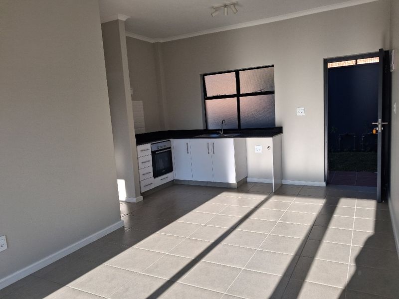 Open-plan kitchen area featuring tiled flooring, built-in cabinetry, oven, and direct access to an outdoor space.