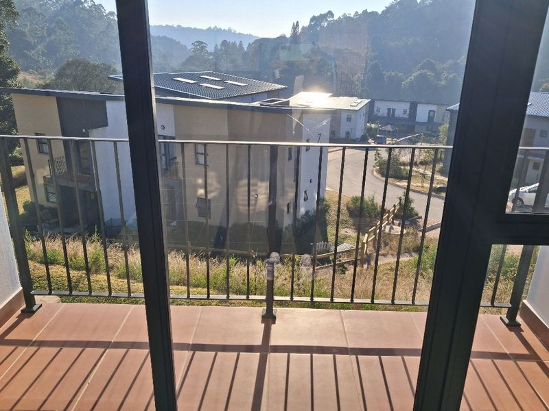 A balcony with tiled flooring and a metal balustrade, offering an elevated view of the surrounding residential estate.