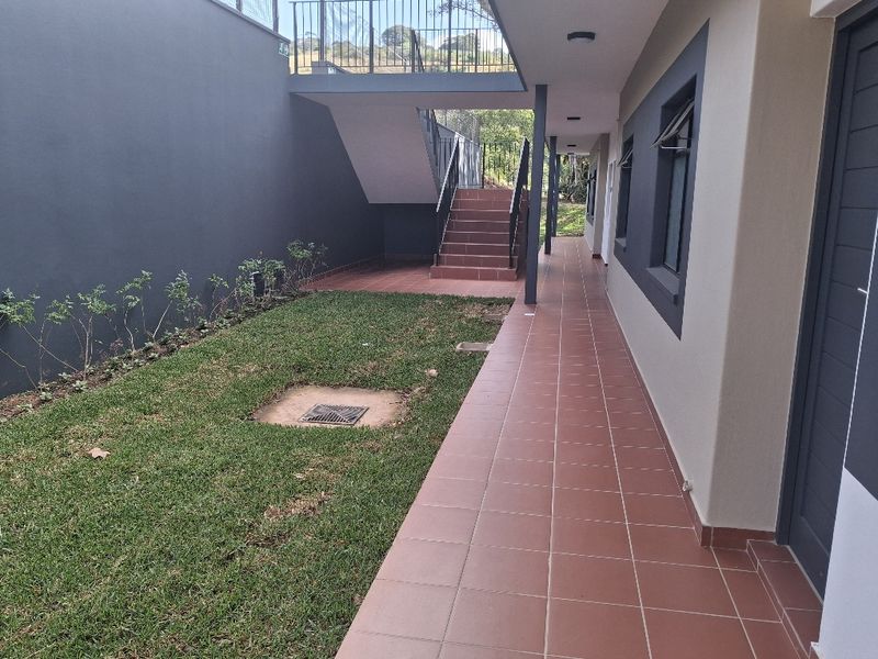 A well-maintained exterior rear area featuring a tiled walkway, a concrete staircase with metal railings, and a small landscaped garden section.