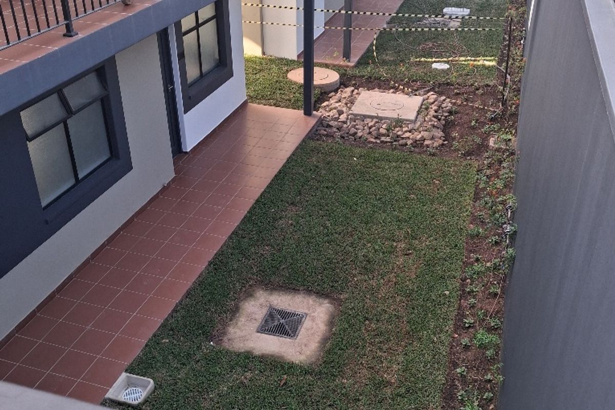 An elevated view of a rear courtyard area featuring tiled patio sections, lawn, and ongoing construction work with scaffolding visible.