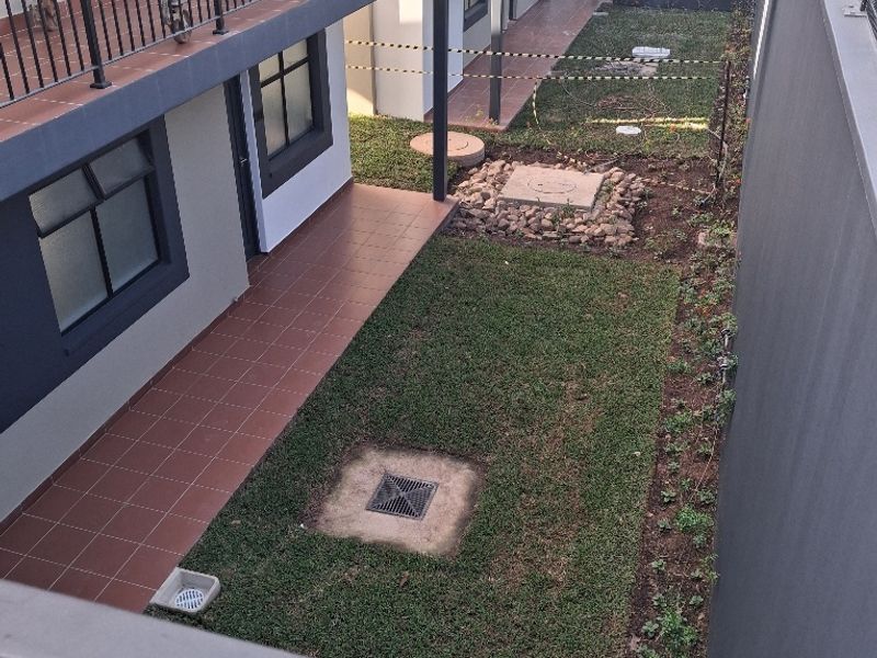 An elevated view of a rear courtyard area featuring tiled patio sections, lawn, and ongoing construction work with scaffolding visible.
