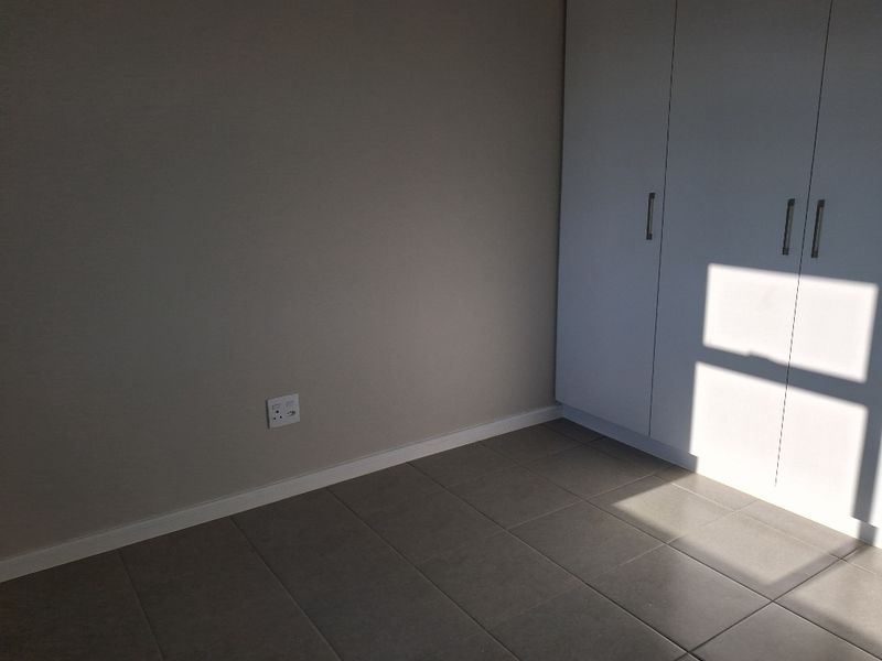 A clean, empty bedroom featuring neutral tiled flooring, built-in white cupboards, and a simple, modern finish.