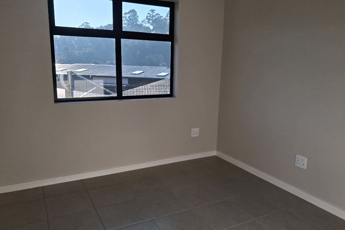 A clean, empty bedroom featuring neutral wall paint, modern grey floor tiles, and a large window providing natural light.