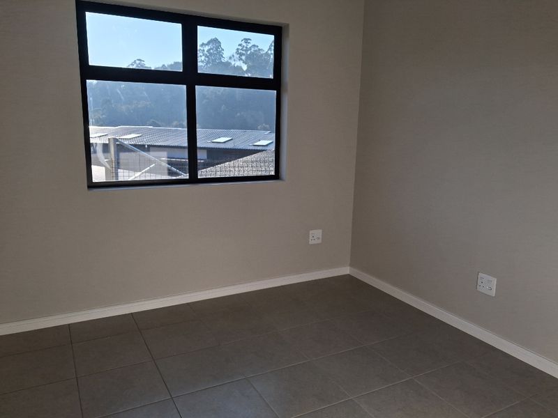 A clean, empty bedroom featuring neutral wall paint, modern grey floor tiles, and a large window providing natural light.