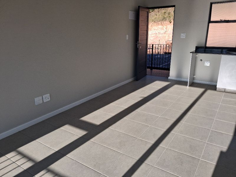 An open-plan living area featuring neutral tiled flooring, a kitchen counter section, and direct access to an outdoor balcony area.