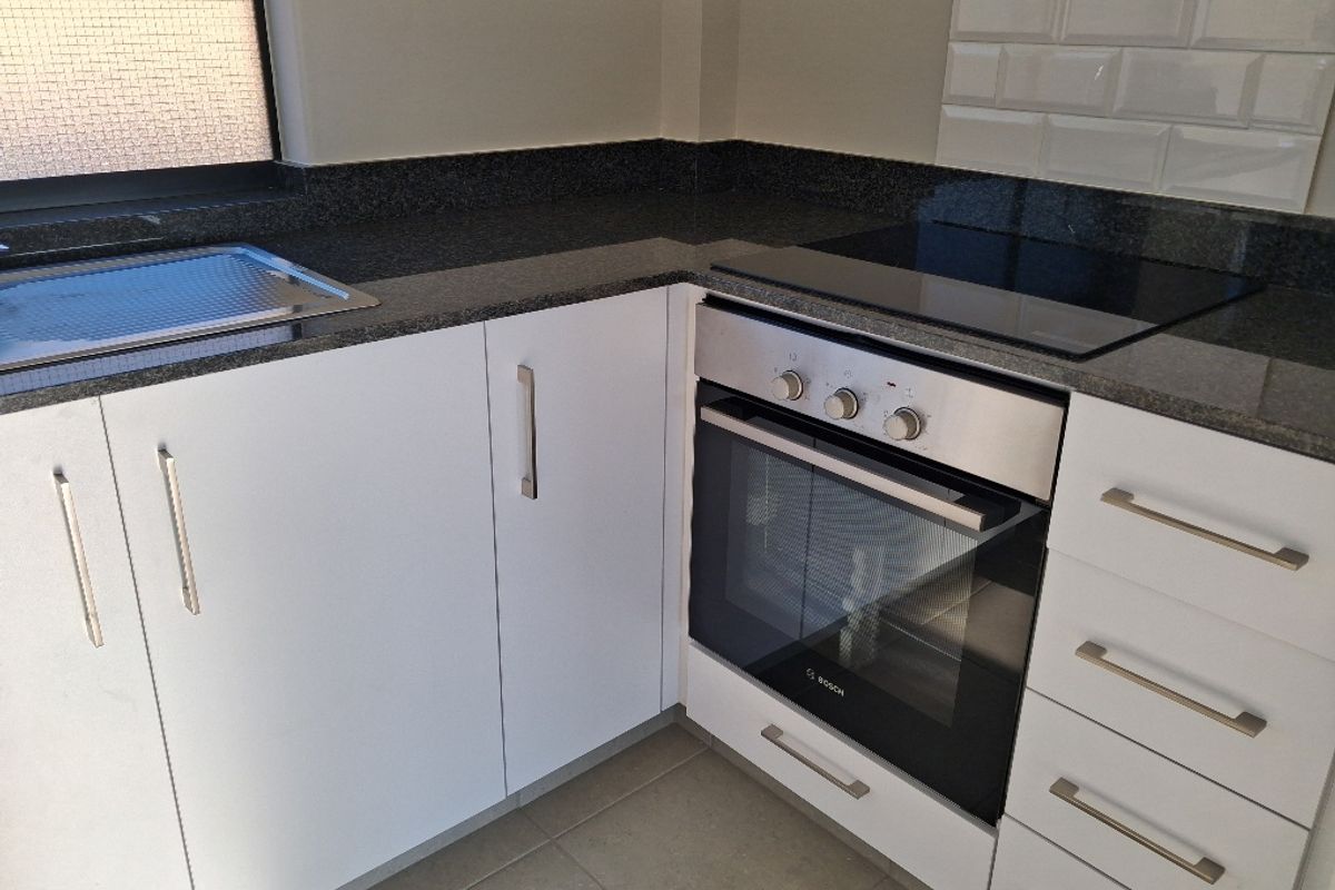 Modern kitchen featuring white cabinetry, granite countertops, subway tile backsplash, and integrated Bosch oven with electric hob.