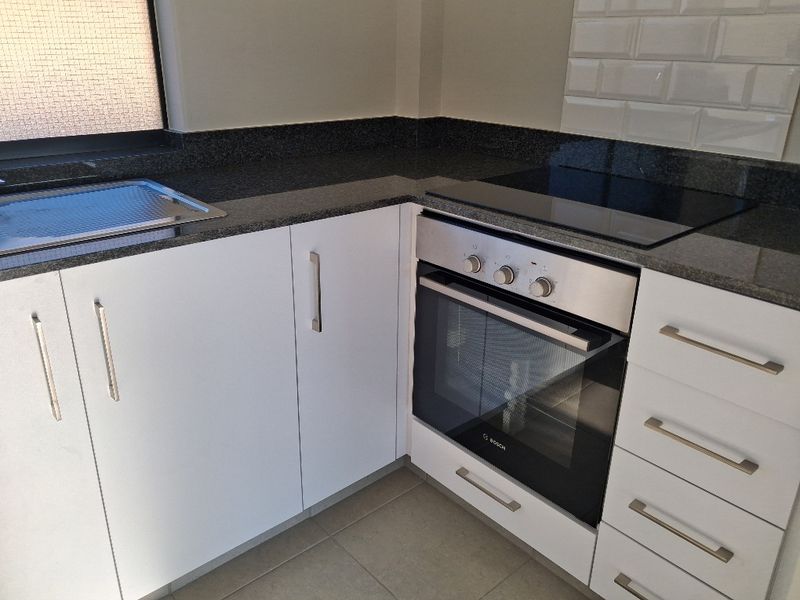 Modern kitchen featuring white cabinetry, granite countertops, subway tile backsplash, and integrated Bosch oven with electric hob.