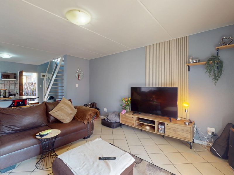 Open-plan living area featuring tiled flooring, a staircase, and decorative slatted wall paneling, seamlessly connecting to the kitchen space.
