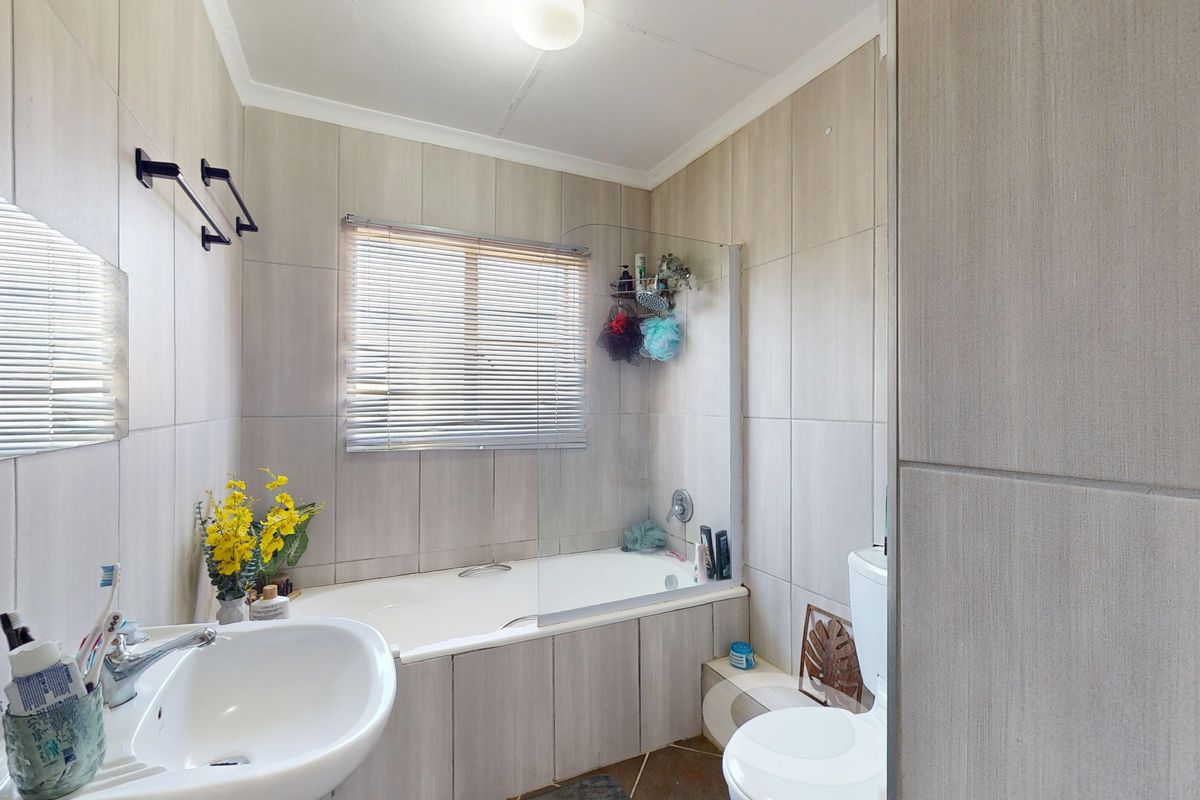 A functional bathroom featuring a built-in bathtub with a glass shower screen, pedestal washbasin, toilet, and neutral wall tiling.
