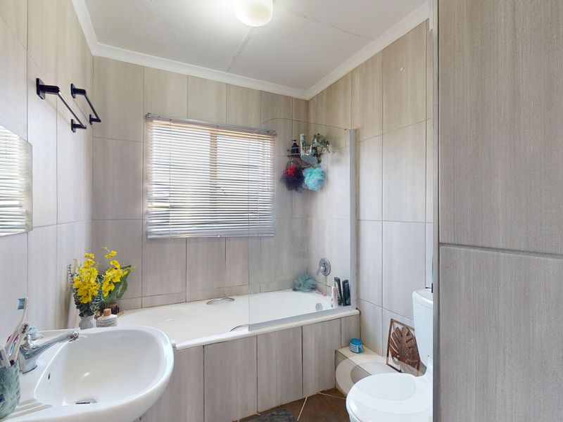 A functional bathroom featuring a built-in bathtub with a glass shower screen, pedestal washbasin, toilet, and neutral wall tiling.
