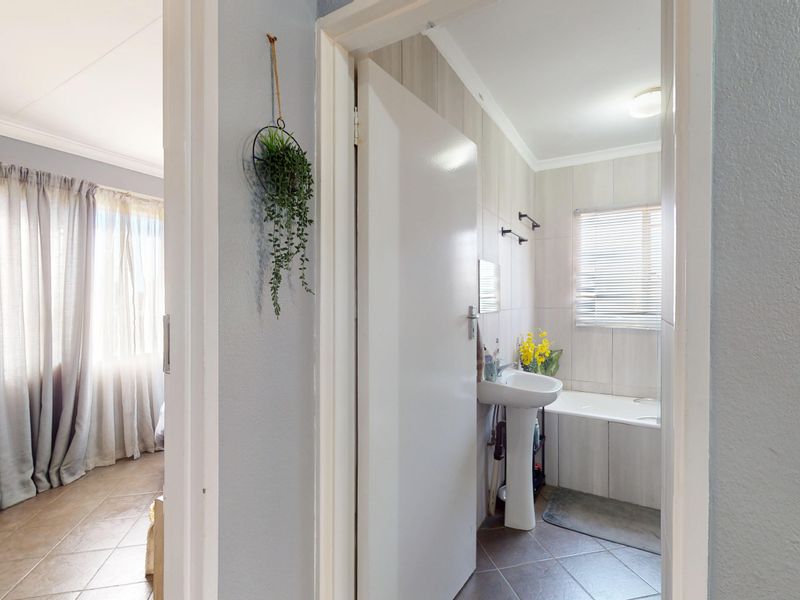 A view from the hallway looking into a bathroom featuring a pedestal basin and a built-in bathtub with tiled finishes.