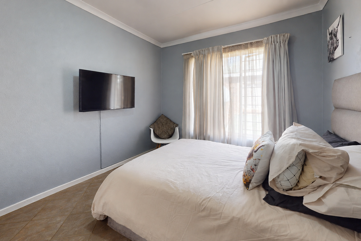 A bedroom featuring tiled flooring, cove cornicing, and a wall-mounted television point with natural light provided by a window with curtain tracks.