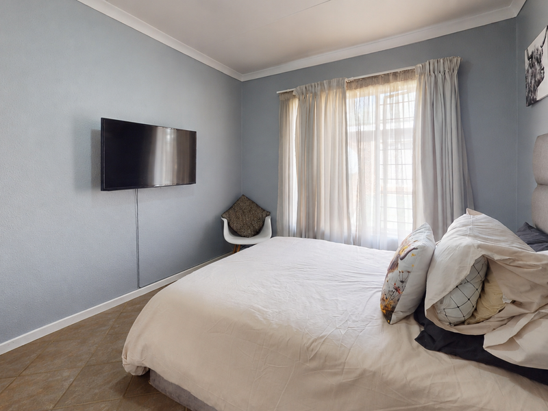 A bedroom featuring tiled flooring, cove cornicing, and a wall-mounted television point with natural light provided by a window with curtain tracks.