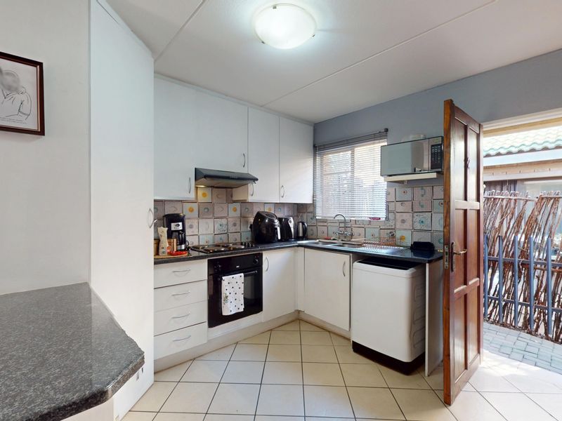 Compact kitchen featuring white cabinetry, built-in oven and hob, tiled backsplash, and direct access to an outdoor area.
