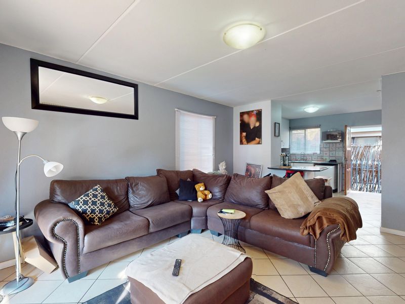 Open-plan living area featuring tiled flooring and a connected kitchen space with built-in cabinetry and appliances.