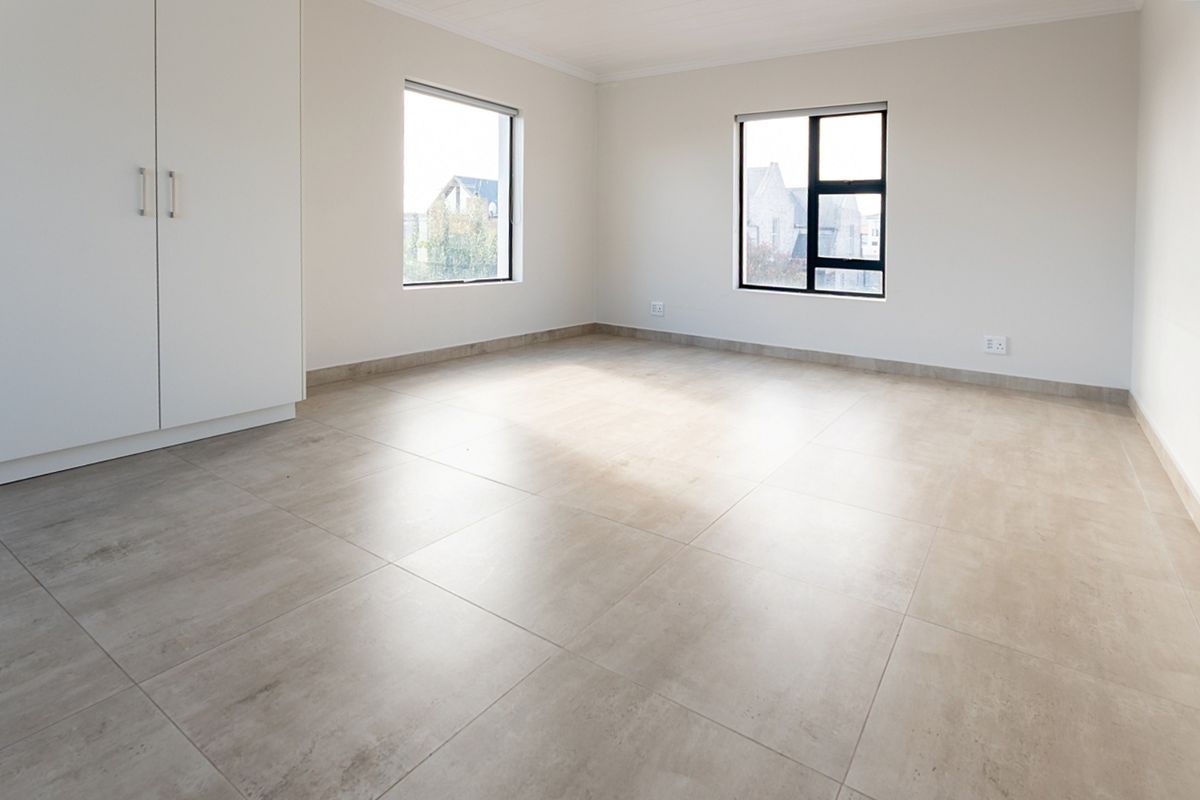 A bright, empty bedroom featuring neutral tiled flooring, built-in cupboards, and large windows providing natural light.