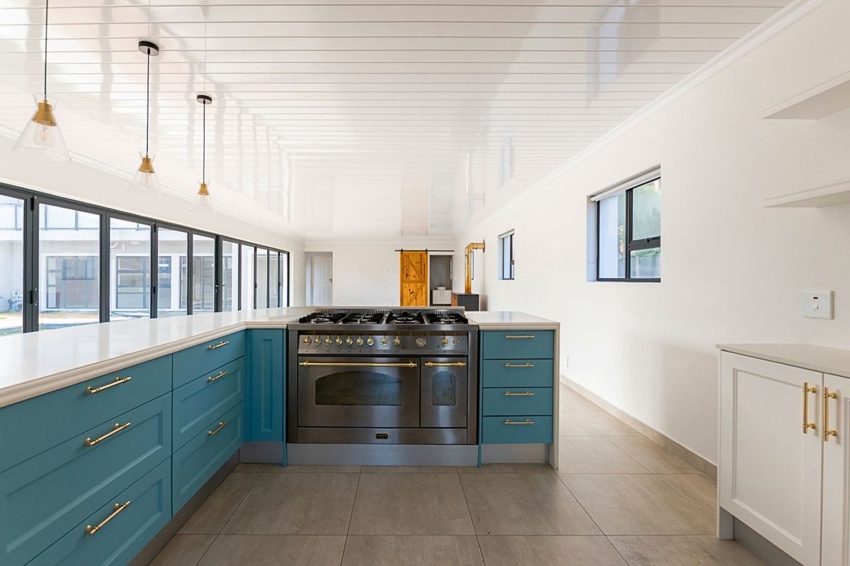 Modern kitchen featuring blue shaker cabinetry, quartz countertops, a professional-grade gas range cooker, and large sliding glass doors opening to the exterior.