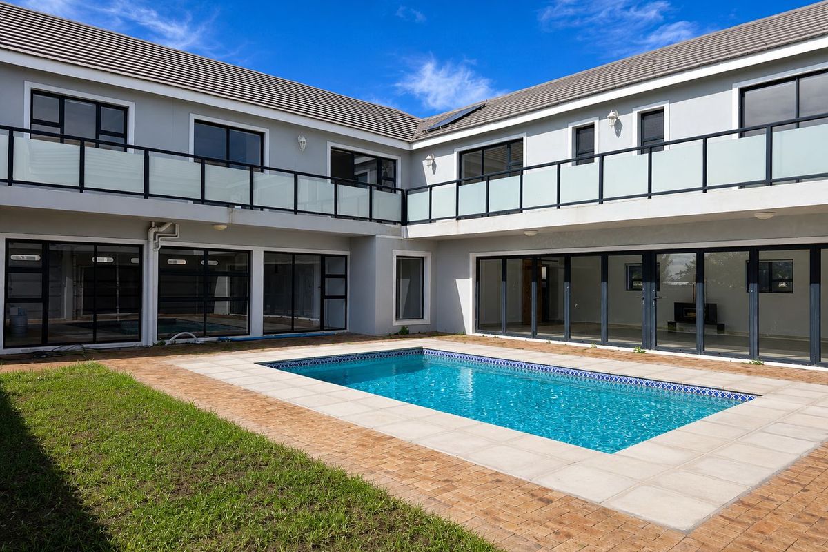 Rear view of a modern two-story home featuring a swimming pool, paved patio area, and upper-level balconies with glass balustrades.